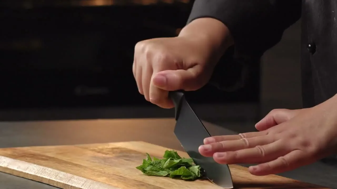 Mani che tagliano erbe su un tagliere, da una produzione Fornace
